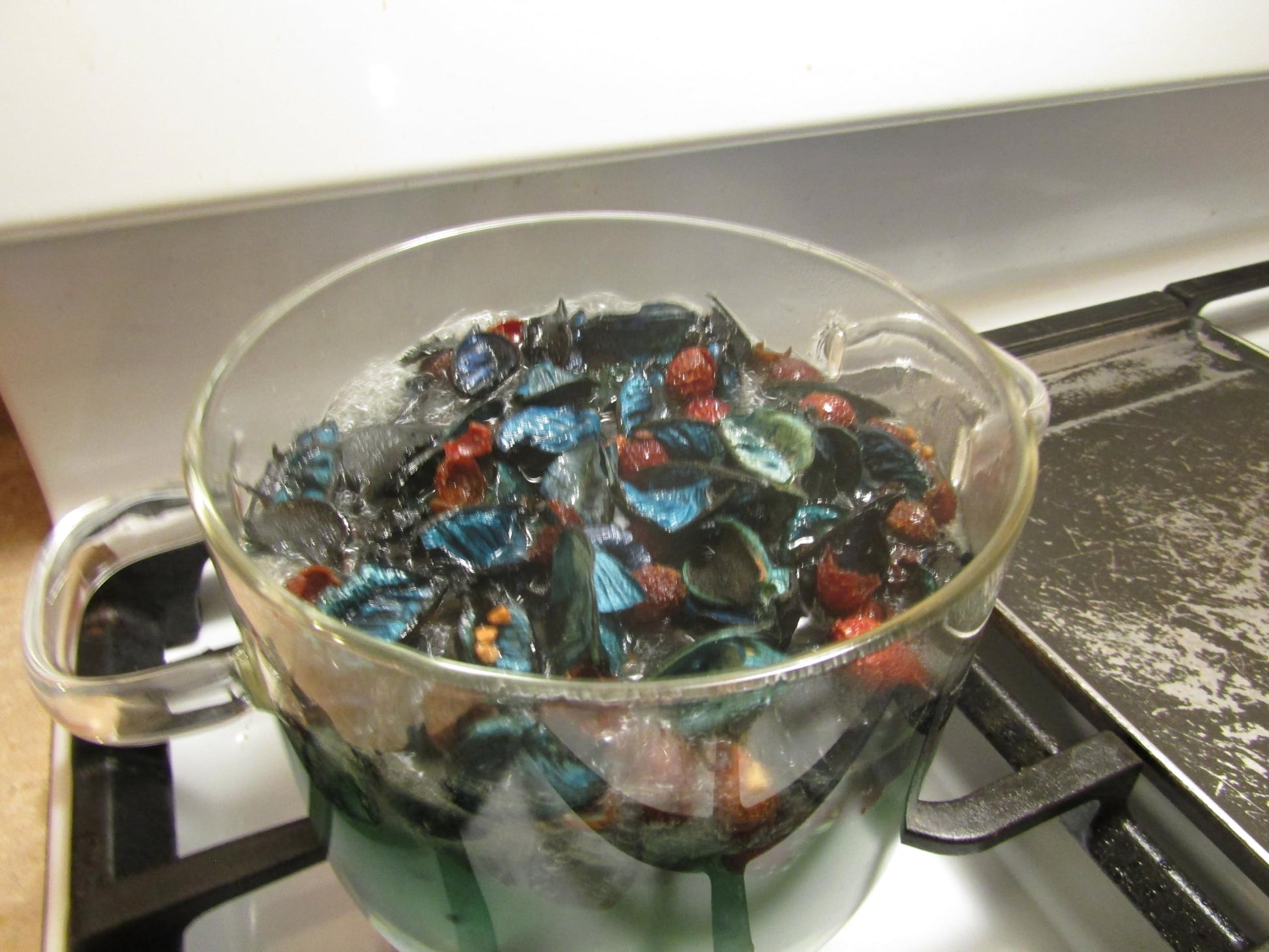 Clear glass pot simmering herbal simmering potpourri with colorful dried herbs on stove burner