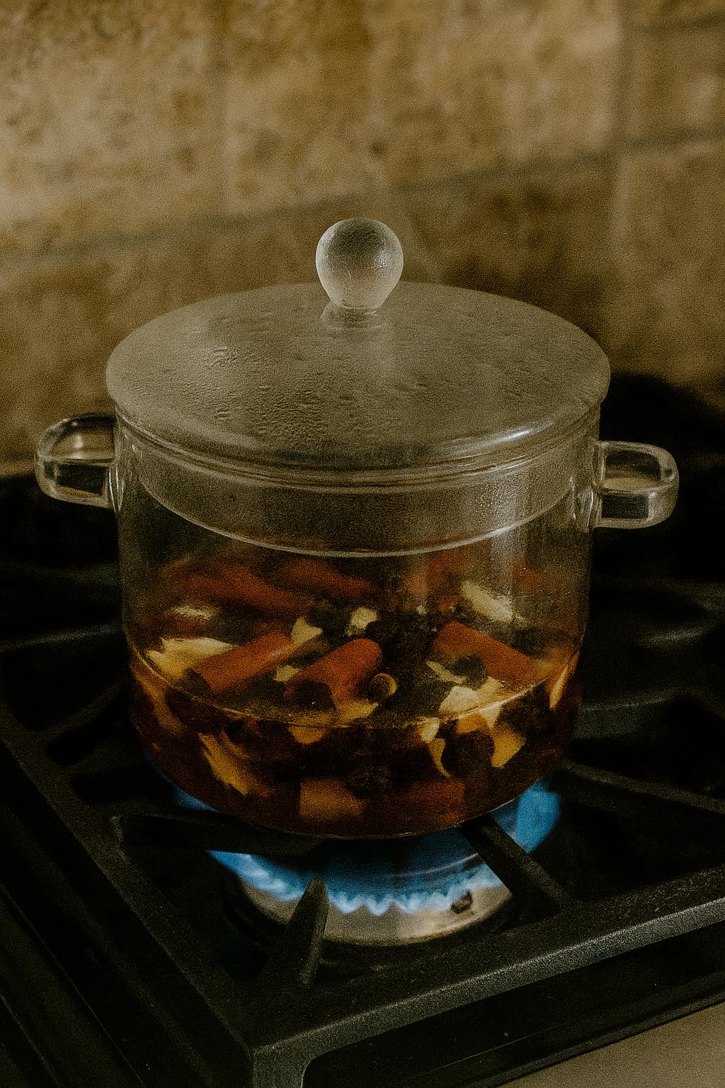 Glass pot simmering on stove containing spiced vanilla simmer potpourri with fragrant spices