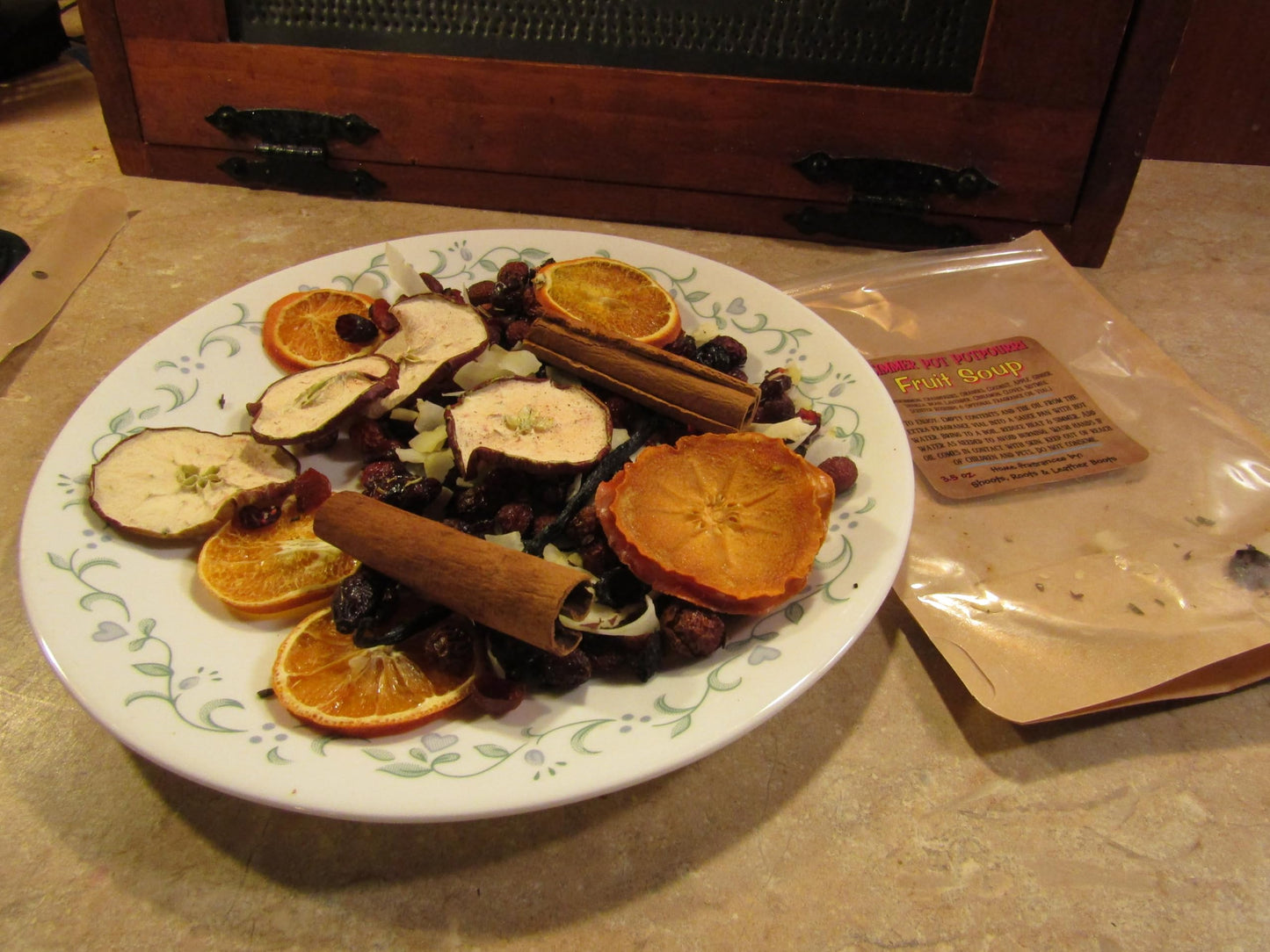 Simmering potpourri with oil on a decorative white plate featuring dried orange slices, cinnamon sticks, and other natural elements