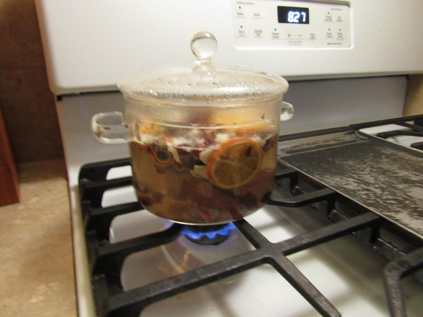 Glass pot on stove with simmering potpourri with oil releasing fragrance and visible fruit slices