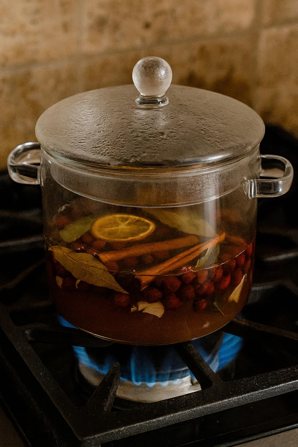 Glass pot with spiced cranberry simmer potpourri simmering on the stove, featuring citrus and spices
