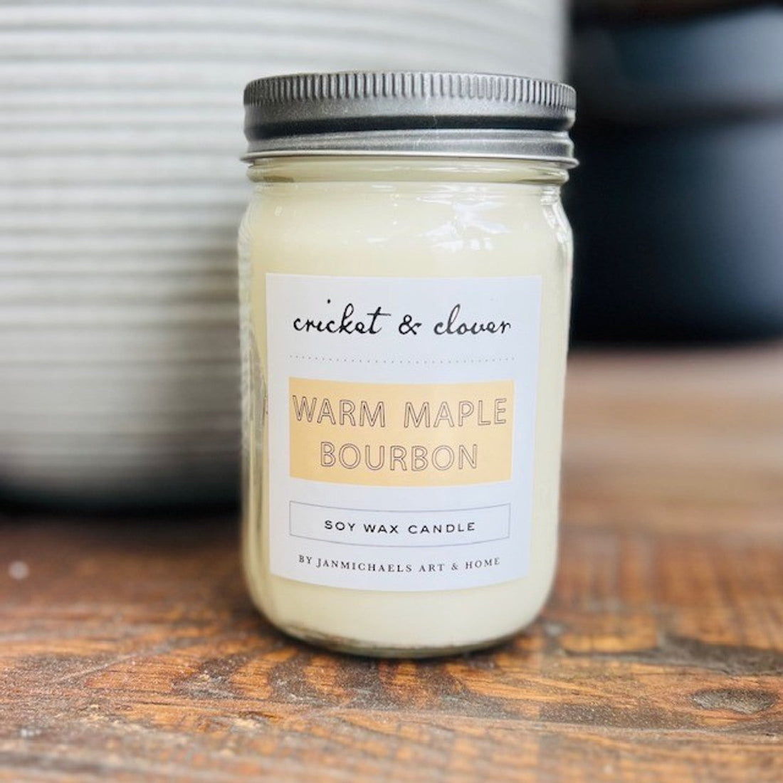 Warm maple bourbon scented candle in a glass jar with metal lid on wooden surface