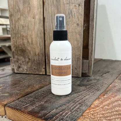 Cricket & Clover Chocolatier Shoppe gourmet room spray in white bottle with black spray top on wooden surface