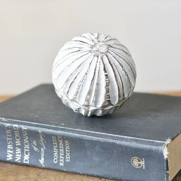 Rustic carved wooden decorative ball in white finish sitting on a vintage Webster's dictionary book