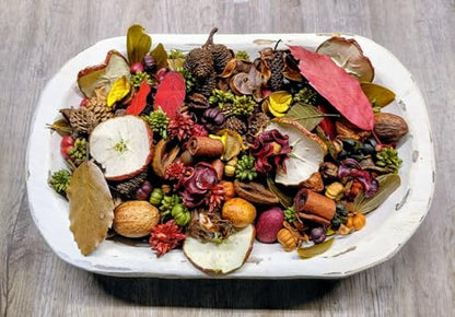 White wooden bowl of rustic autumn potpourri handmade with dried apple slices nuts cinnamon pods pine cones and leaves