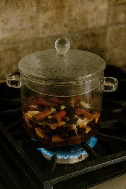 Glass pot simmering on stove containing spiced vanilla simmer potpourri with fragrant spices