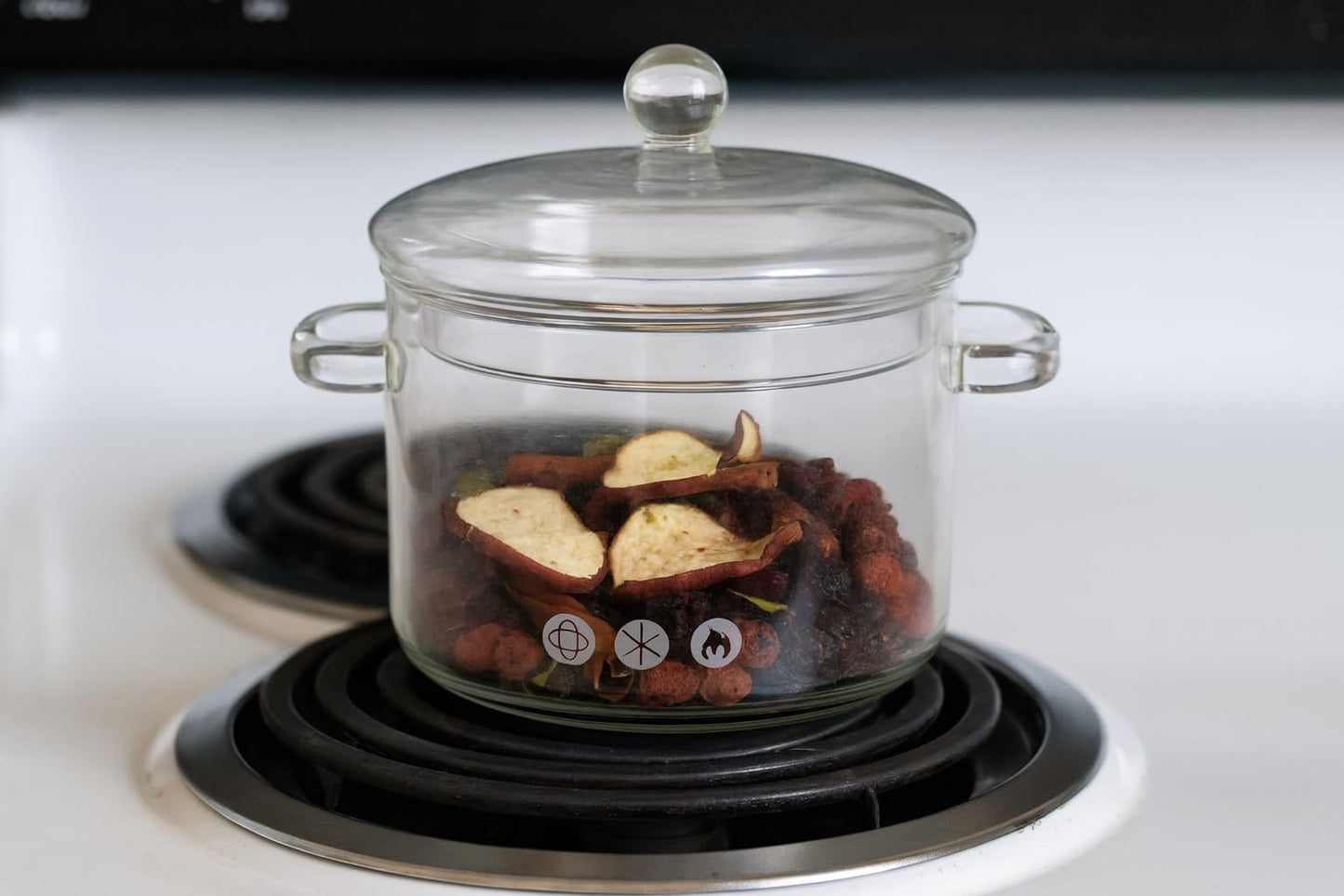 Glass pot on electric stove containing dried apple slices and spices for apple pie simmer potpourri