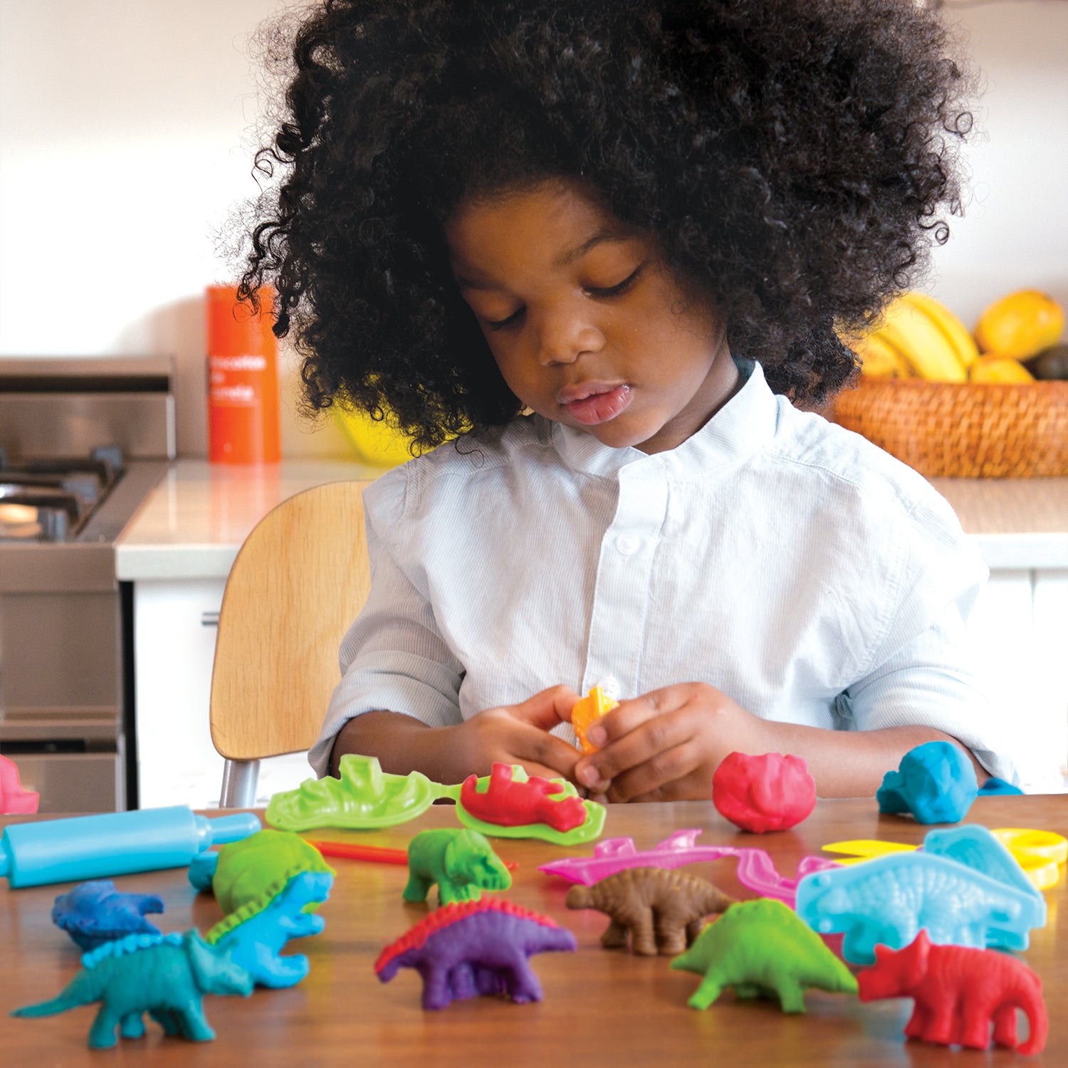 Child playing with colorful dinosaur modeling dough kit and dinosaur molds on a wooden table