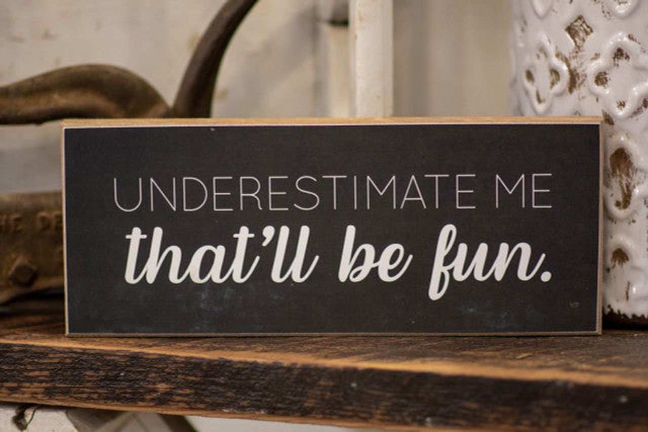 Black wooden home decor sign with white text underestimate me that will be fun sign on rustic shelf
